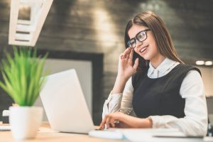 The cheerful woman with a modern laptop sitting at the desktop