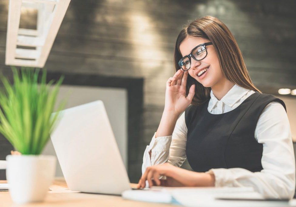 The cheerful woman with a modern laptop sitting at the desktop