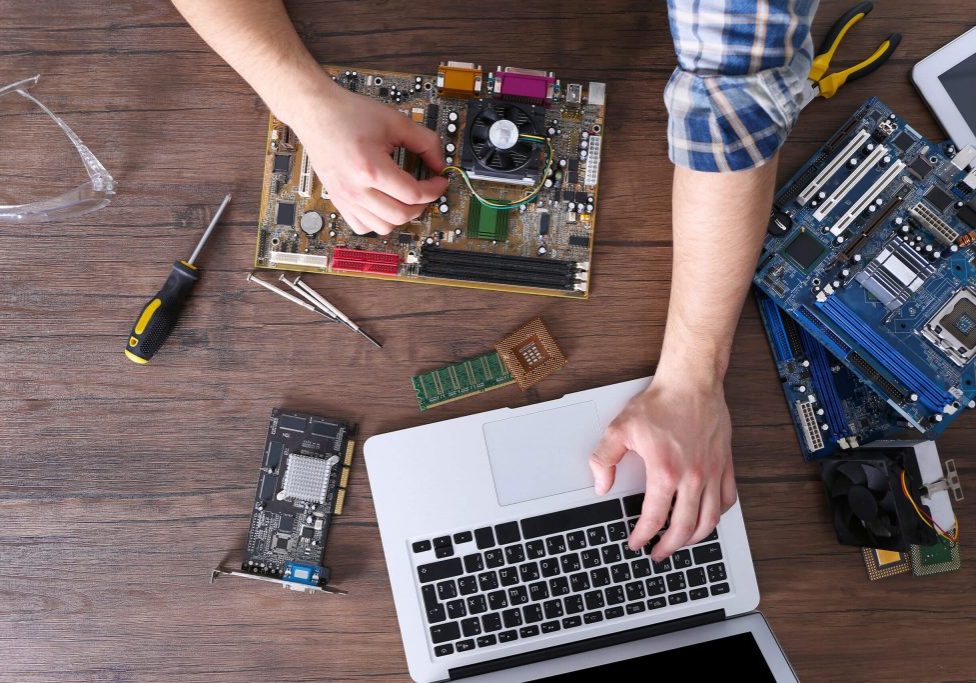 Male hands repairing computer details and using laptop on wooden table